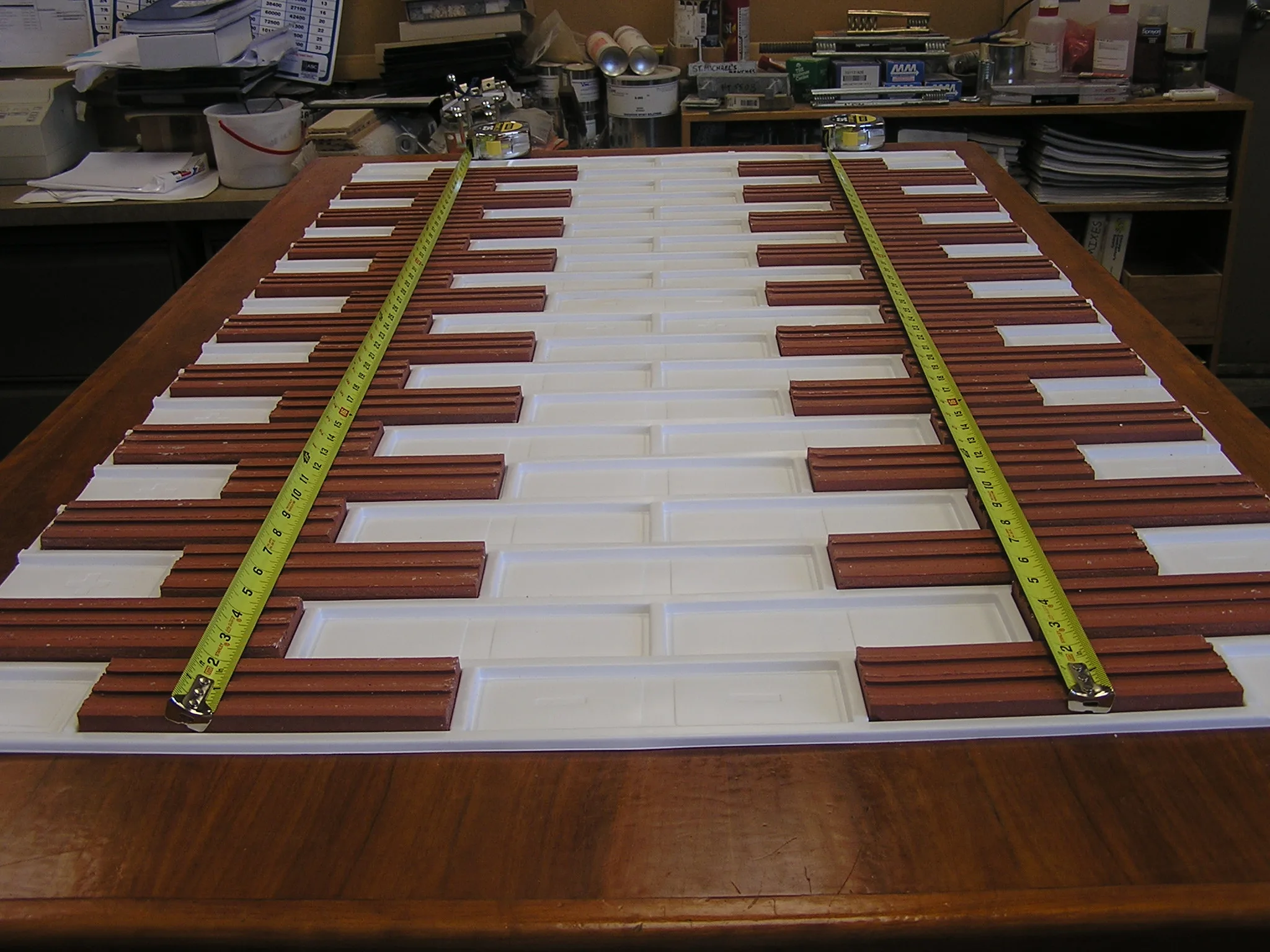 Real clay thin brick laid into the pockets of a white plastic thin brick formliner, with tape measures across the coursing